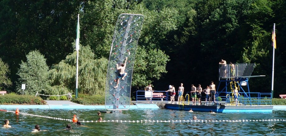 Waldschwimmbad von der Nichtschwimmerweite mit Jugendlichen auf Kletterwand und Sprungturm sowie im Wasser