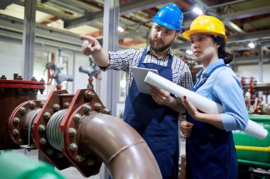 Symbolbild Abwassertechnik: zwei Arbeiter in einer Halle mit Maschinen und einer Pipeline.