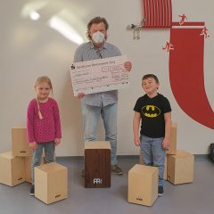 Ein Erzieher und Kinder der Kita Hamm präsentieren den erhaltenen Scheck und von den Fördermitteln angeschafften Cajons.