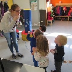 Eine Erzieherin bläst Seifenblasen in die Luft. Kinder schauen ihnen gebannt hinterher.
