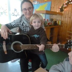 Musik spielt eine große Rolle. Hier hat eine Erzieherin ein Kind und eine Gitarre auf dem Schoß.